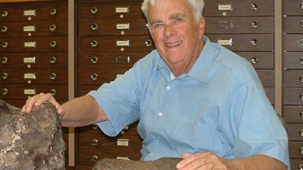 ASU Emeritus Regents Professor Carleton Moore smiles in a lab with his hands placed on two meteorites. 