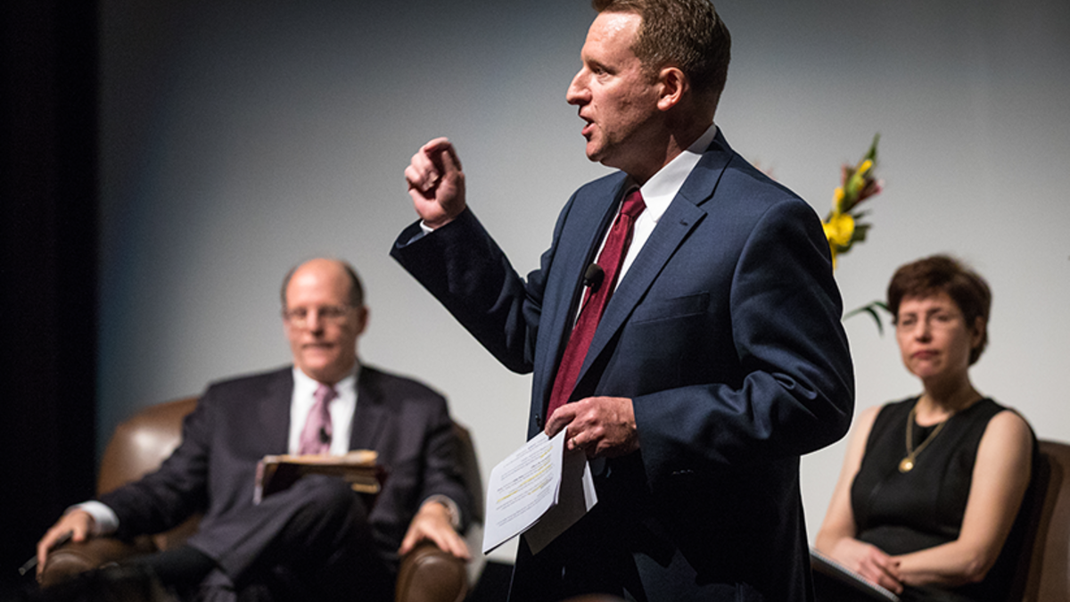 Center director John Carlson, wearing a navy suit and red tie, speaks at a forum regarding politics and religion