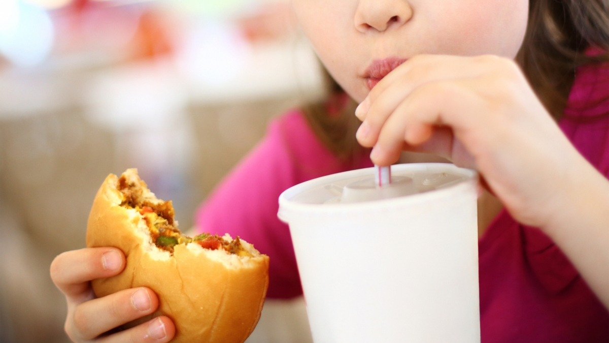 child drinking sugary beverage and eating a hamburger