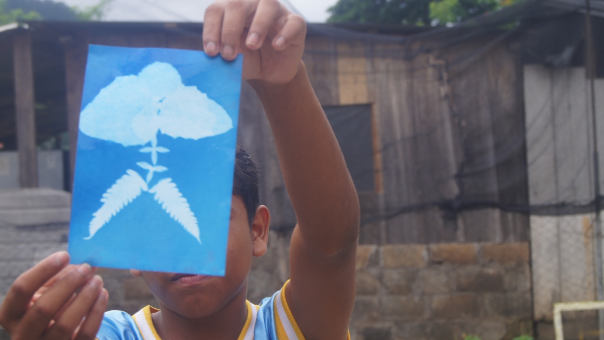 A Honduran child holds up a blue and white cyanotype of a plant