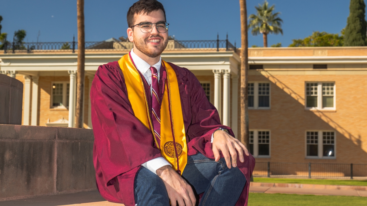 Chris Green in graduation robes sitting on steps at the Tempe campus