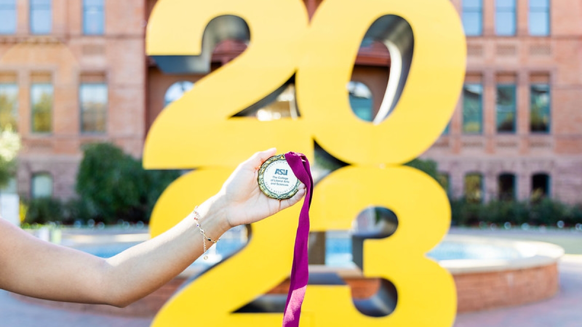 Hand holding a Dean's Medal in front of a large 2023 sign.
