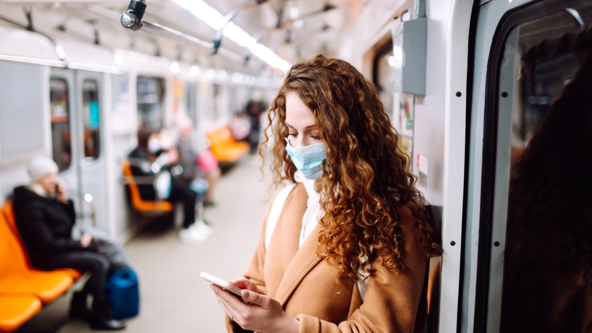 Woman wearing a mask checks her phone while riding public transportation