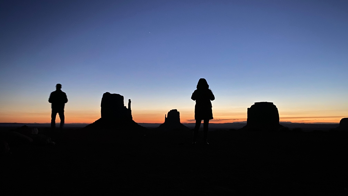 Two people silhouetted against a backdrop of desert scenery.