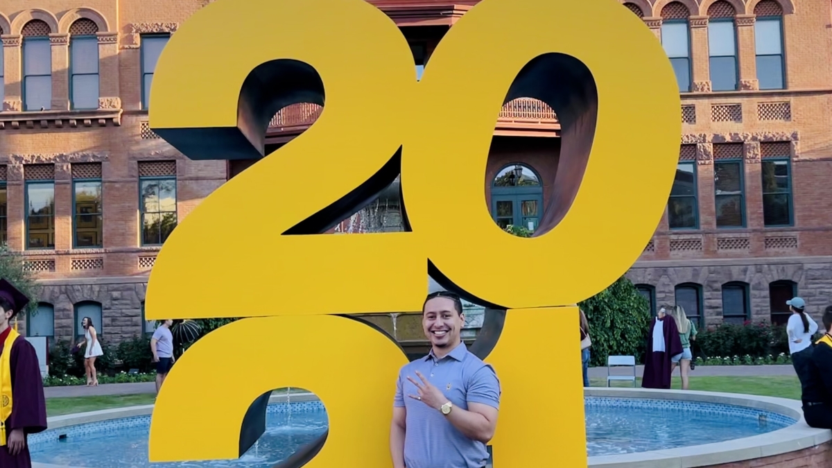 ASU grad Daniel Sanchez in front of a big 2021 statue at Old Main on ASU's Tempe campus
