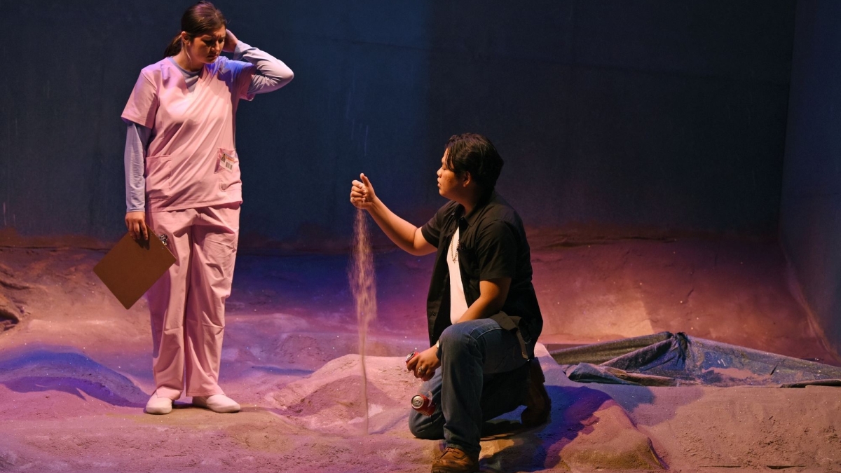 Man kneels with sand flowing through his fingers while a nurse, standing, looks on.