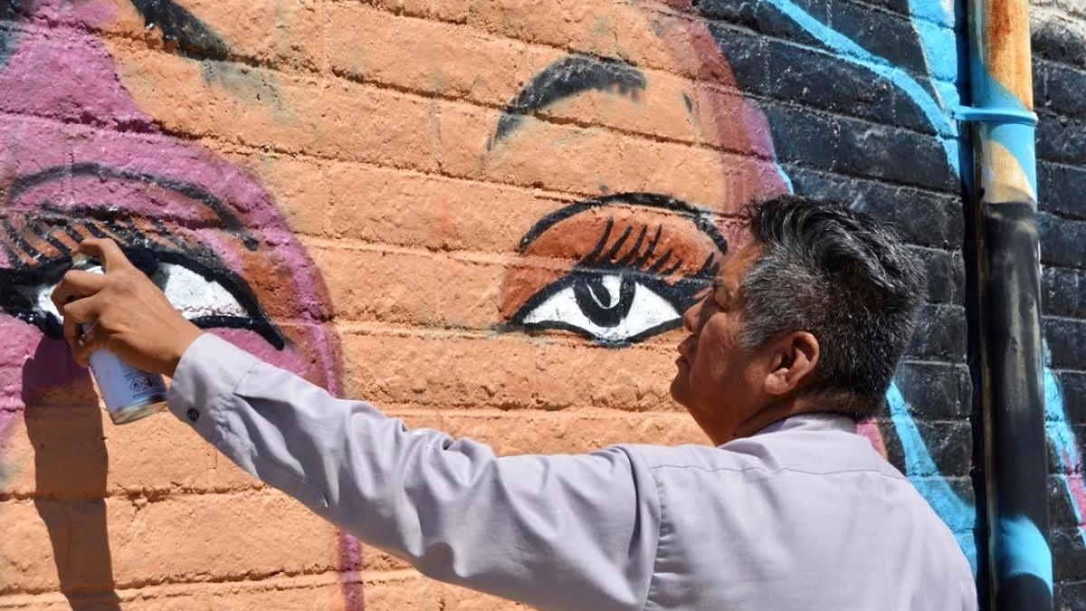 Douglas Miles paining a mural of an Apache woman.