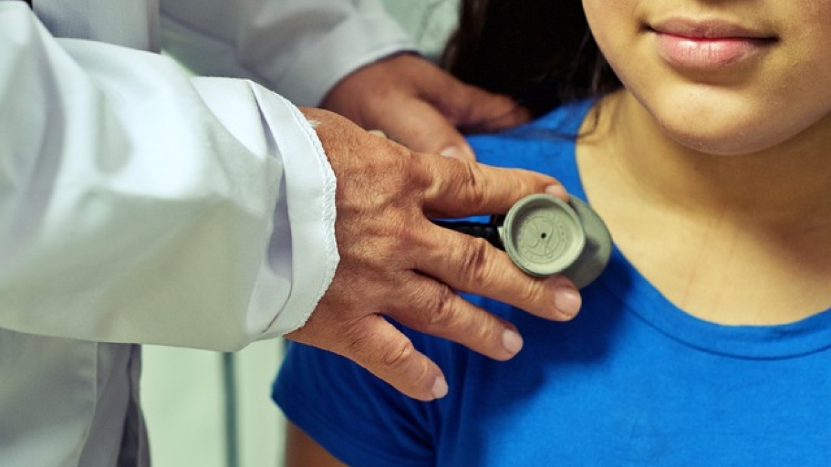 Doctor's hand with a stethoscope against a girl's chest.