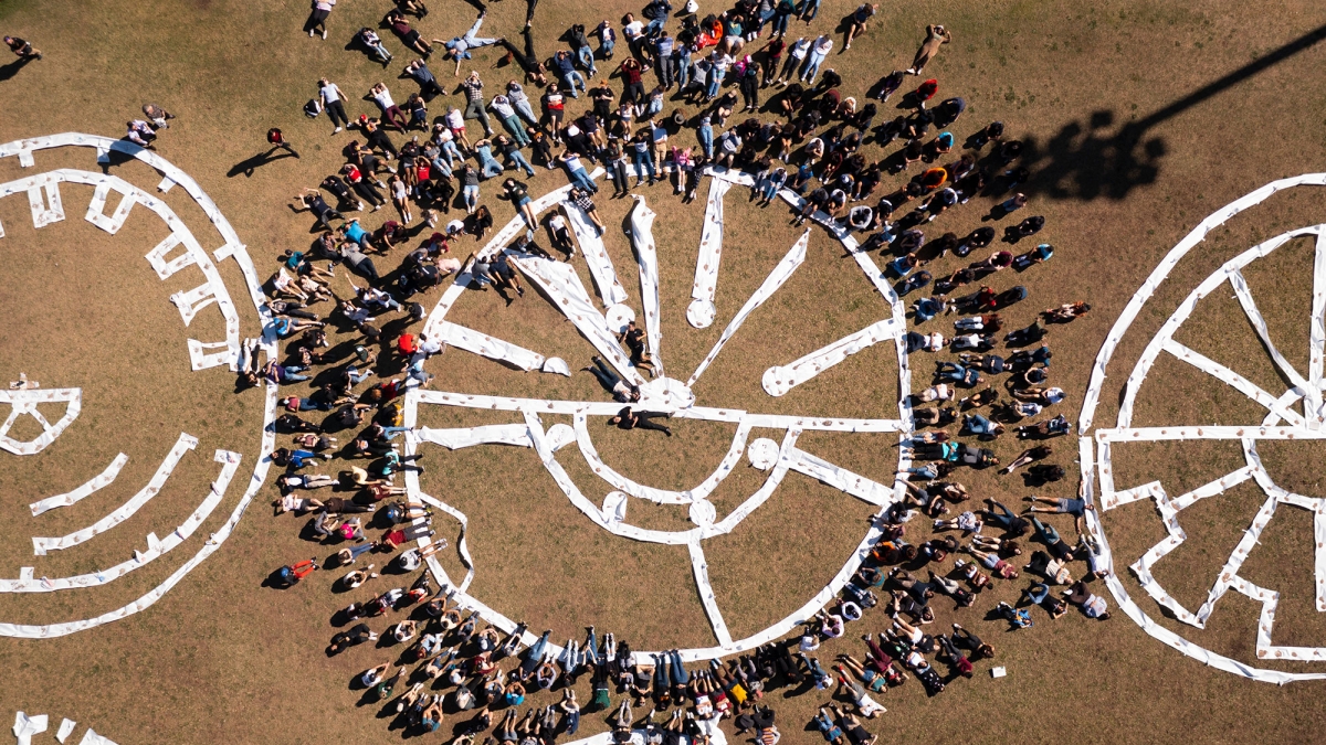 Aerial photo of people surrounding a 50-foot-wide flat, circular sculpture made with paper on field.