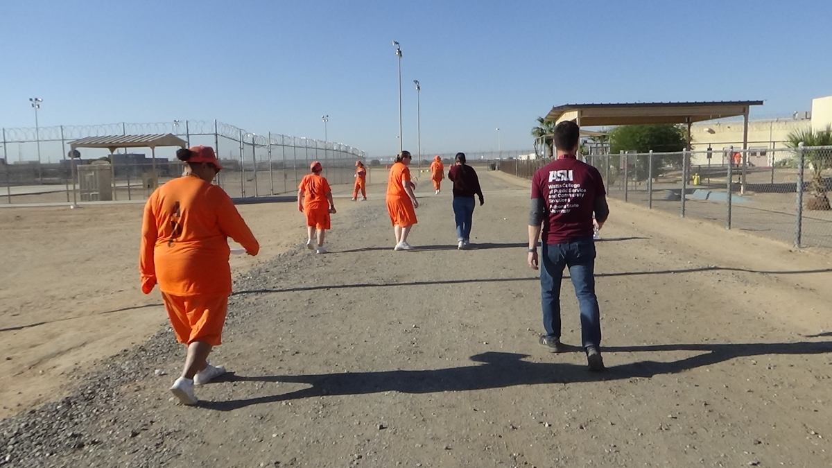 People in orange jumpsuits walk on an outdoor track.
