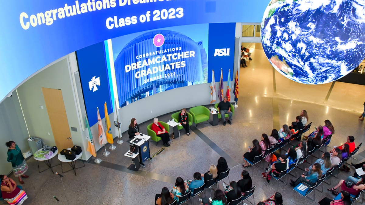 A group of people gathered in a room, sitting in chairs, with a digital sign above that says "Congratulations DreamCatcher Graduates Class of 2023"