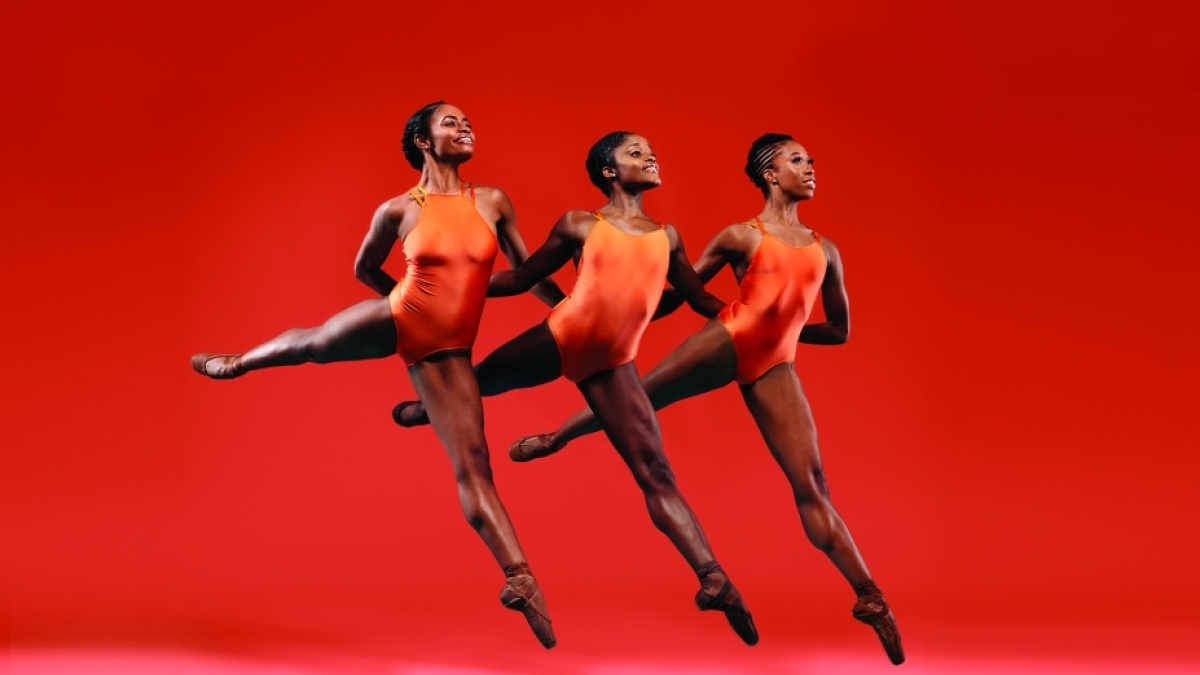 Three ballerinas in orange leotards performing and jumping in unison