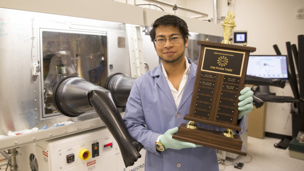 Photo of Sebastian Husein holding a trophy in a lab. 