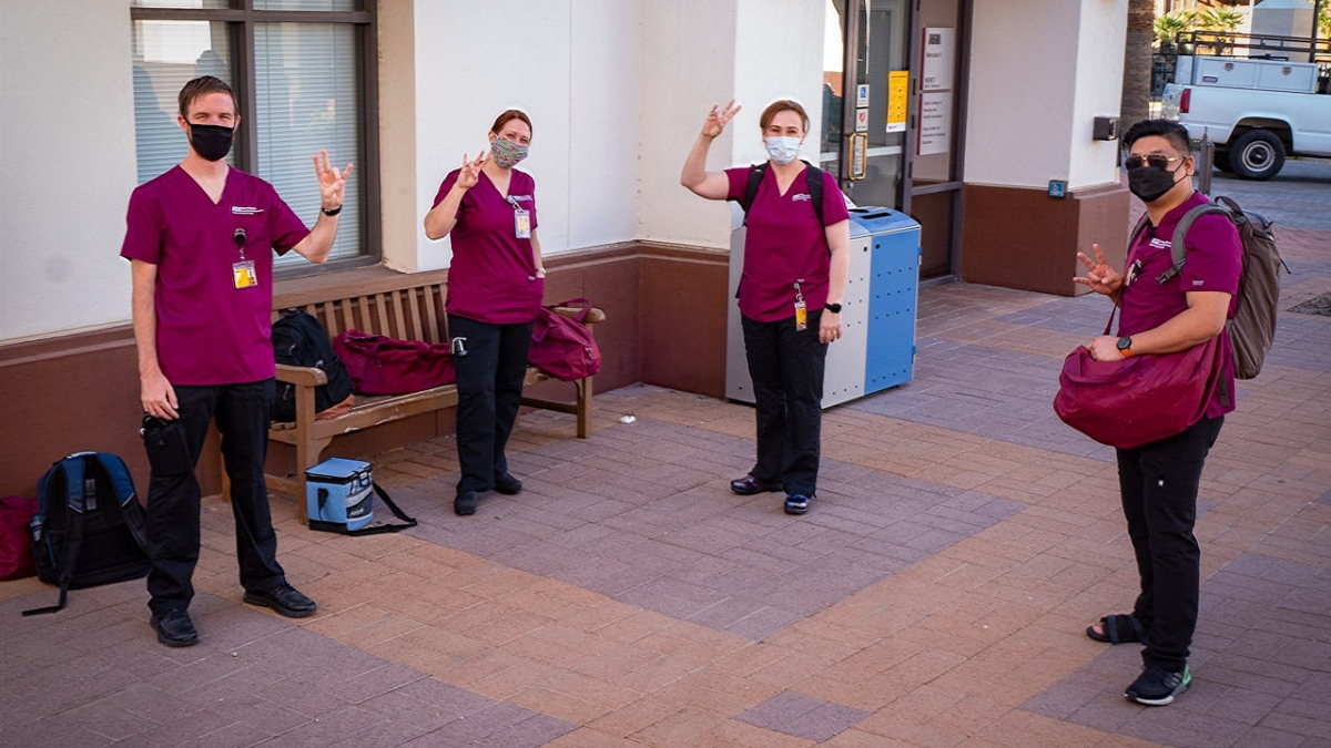 Four nursing students in scrubs and face makss pose for a photo throwing pitch forks