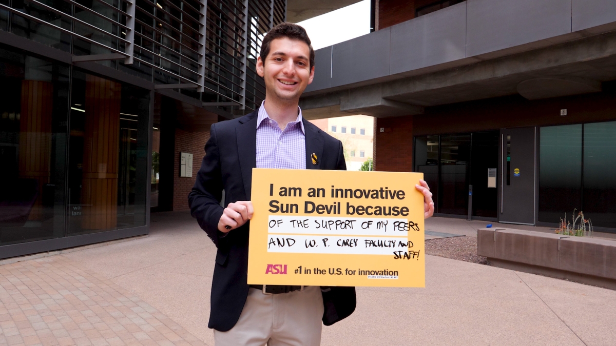 man holding sign that says "I am an innovative Sun Devil because of the support of my peers and W. P. Carey faculty and staff!"