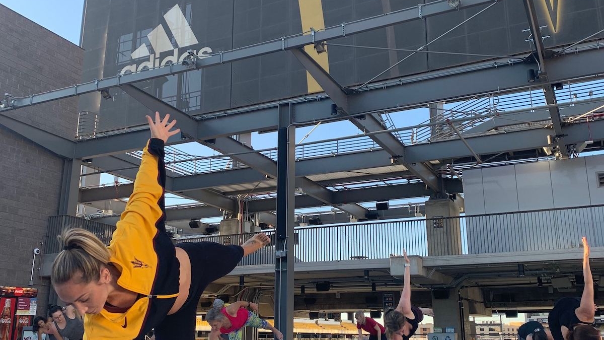 Yoga instructor leads stadium yoga on the sun deck with guests in background