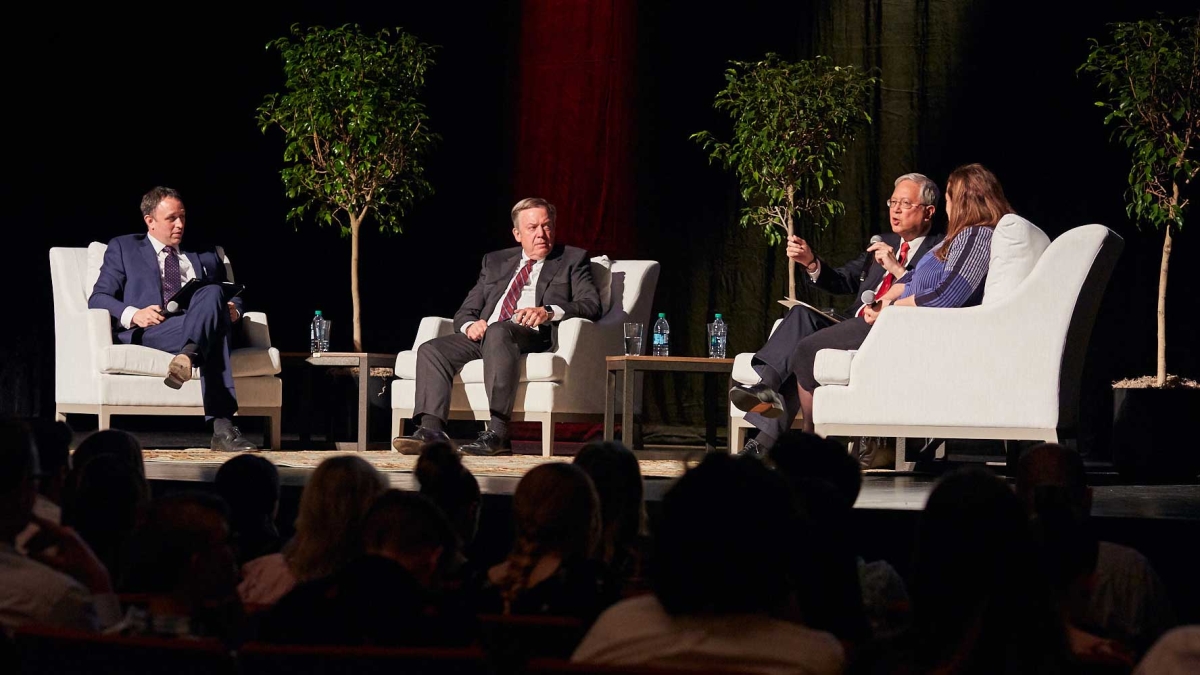 Four panel participants sit in armchairs onstage