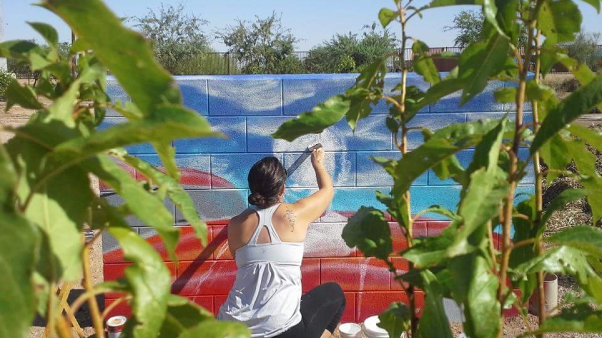 Kira Olsen-Medina painting a mural on a brick wall.