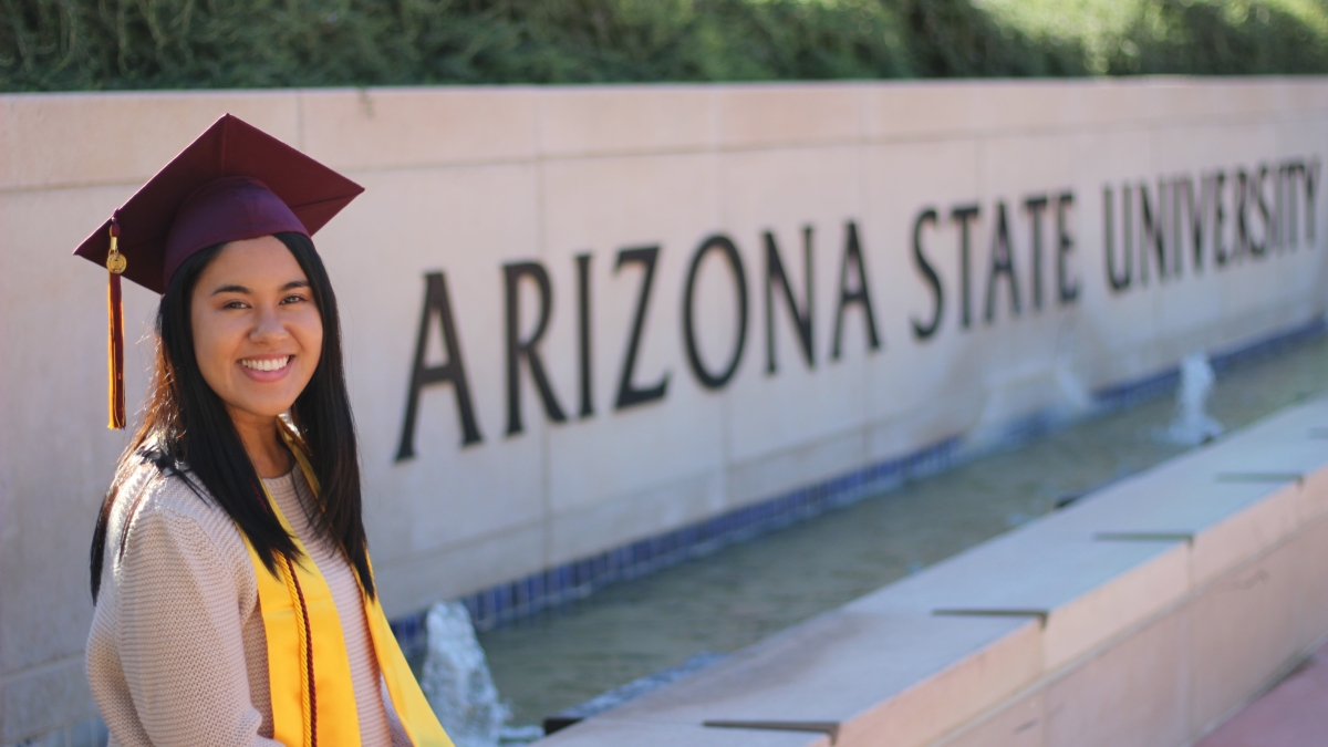 Yvonne Cabrera sitting in her graduation cap in front of ASU sign