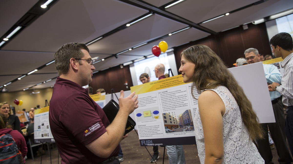 Photo of female student talking with a man in front of a poster with a caption of "Sharing your research and ideas at the FURI Symposium are part of the experience for undergraduate researchers like Emily Ford (right). Photographer: Jessica Hochreiter/ASU