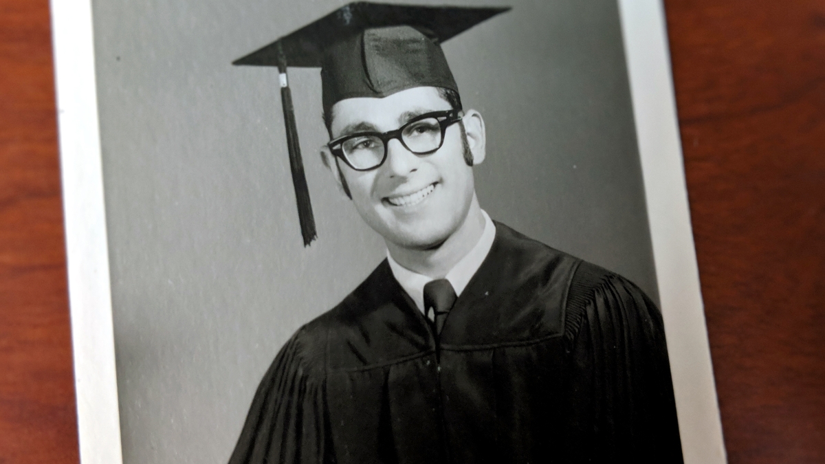 Geoffrey Gonsher graduation photo from 50 yrs ago, wearing black cap and gown and thick, black rimmed glasses