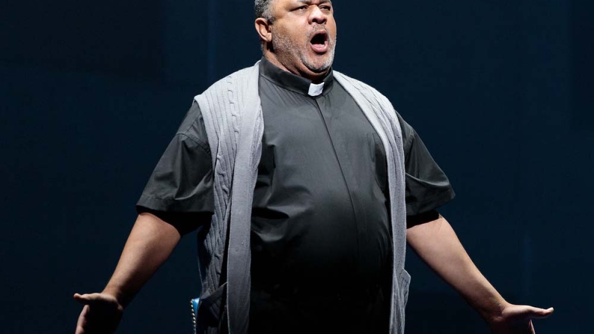 man dressed as a reverend, singing on stage