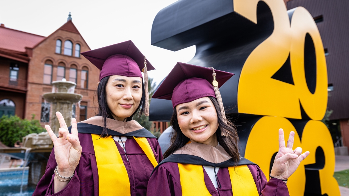 Photo of two graduates in front of Old Main at ASU and a giant 2023 sign.