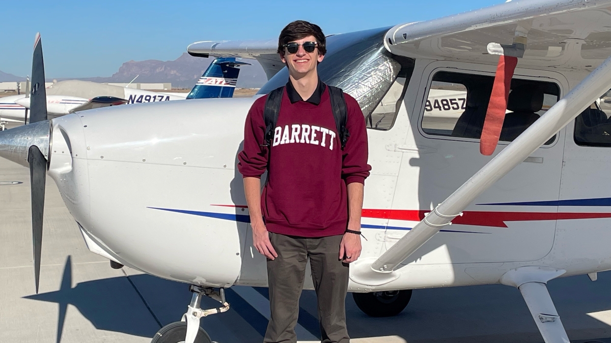 ASU grad Grant Penderghast wearing a maroon sweatshirt that says "Barrett" while standing next to a small airplane.