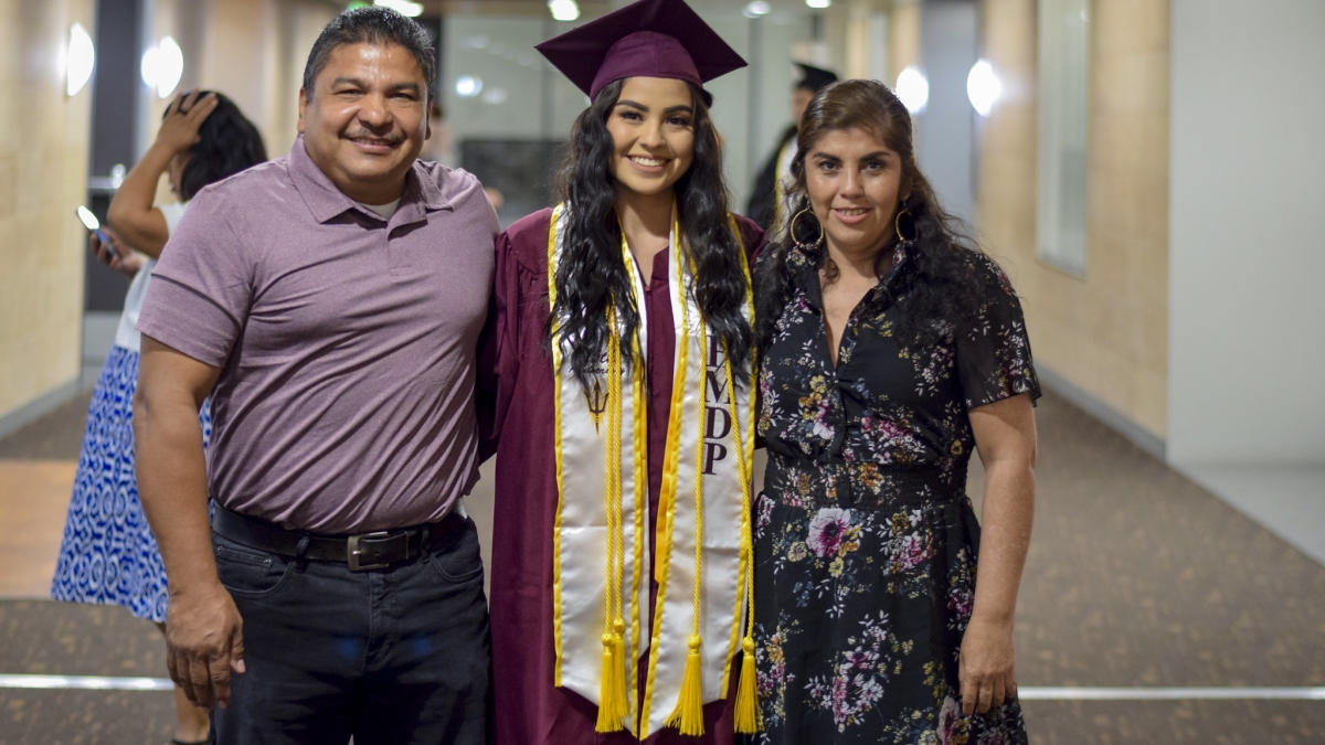 A young woman poses with her parents in her graduation regalia at the Hispanic Mother Daughter Program graduation at ASU