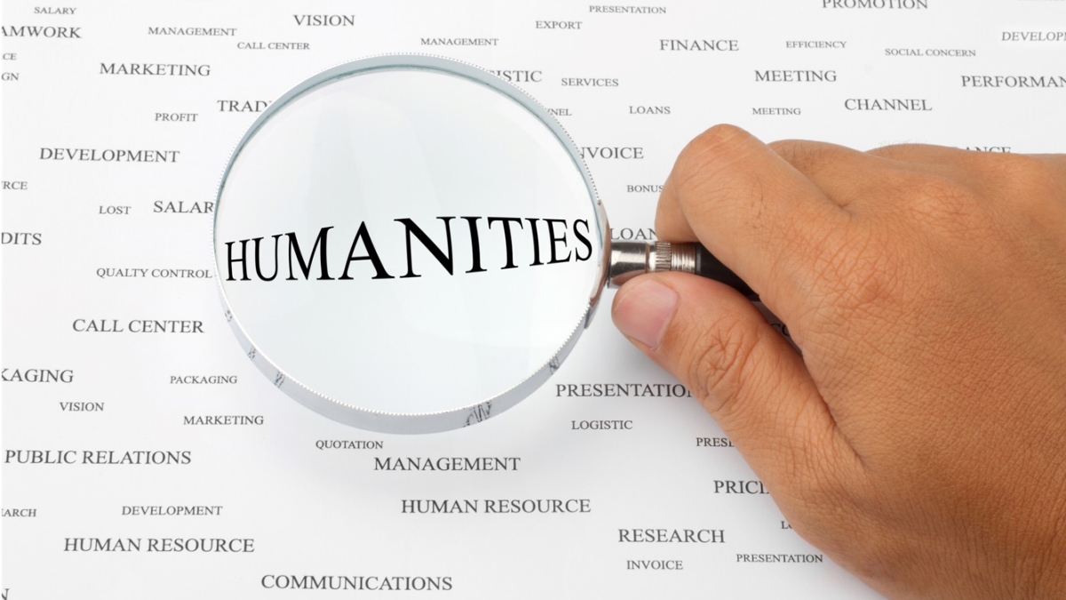Hand holding a magnifying glass hovering over a page with several words on it. The magnifying glass shows the word "humanities."