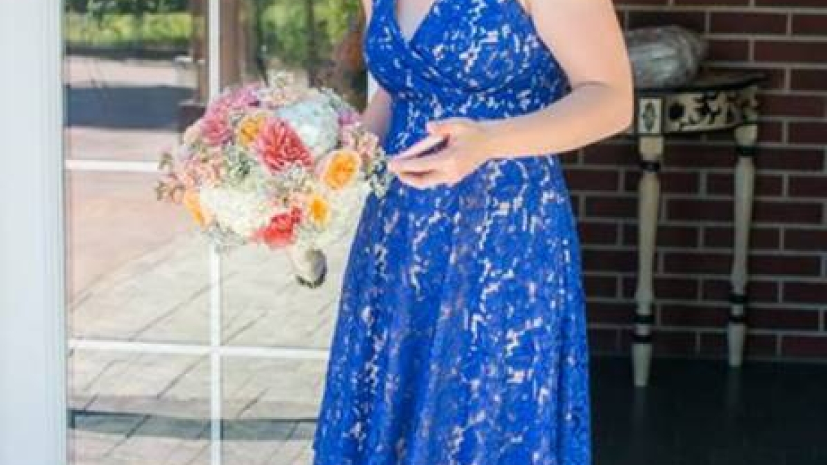 Smiling woman wearing a blue dress and holding a bouquet of flowers.