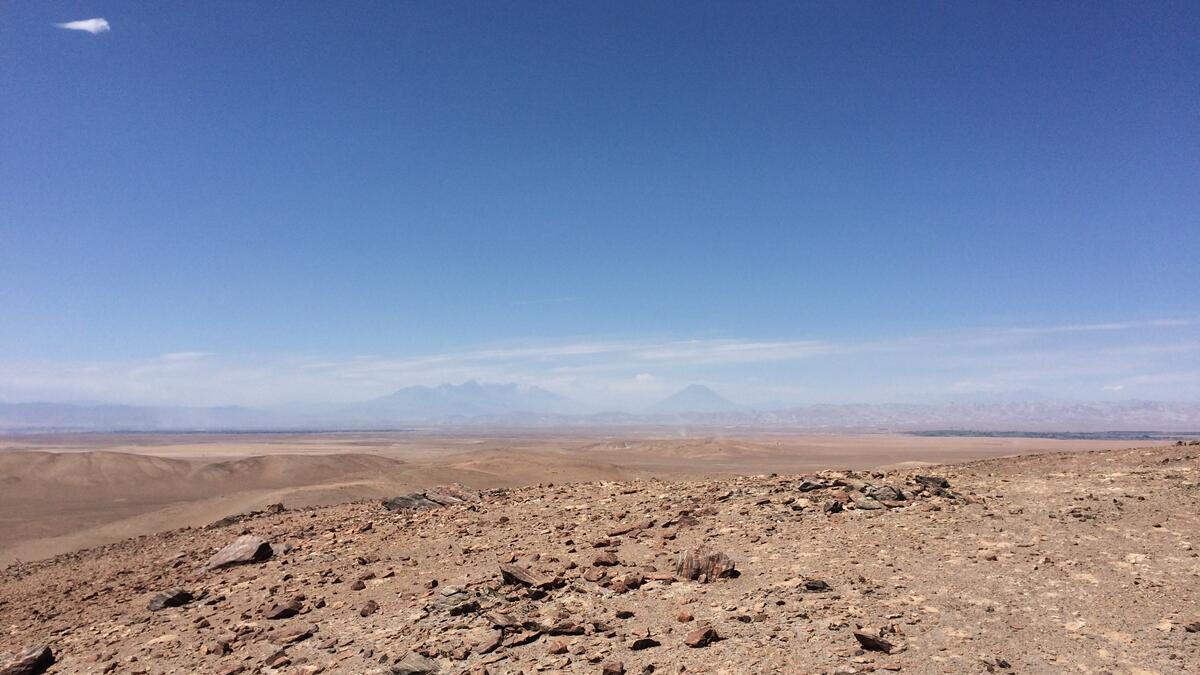 The rugged, flat, dirt of a desert terrain below with a bright blue sky above.