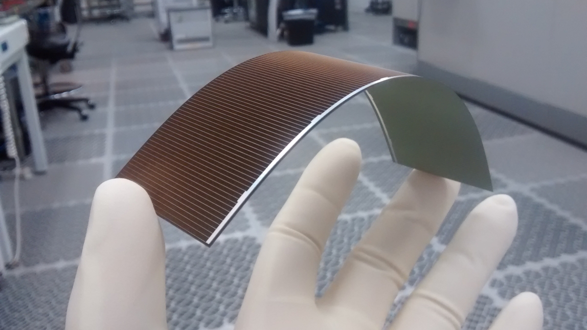 A gloved hand holds a flexible solar cell in a lab.