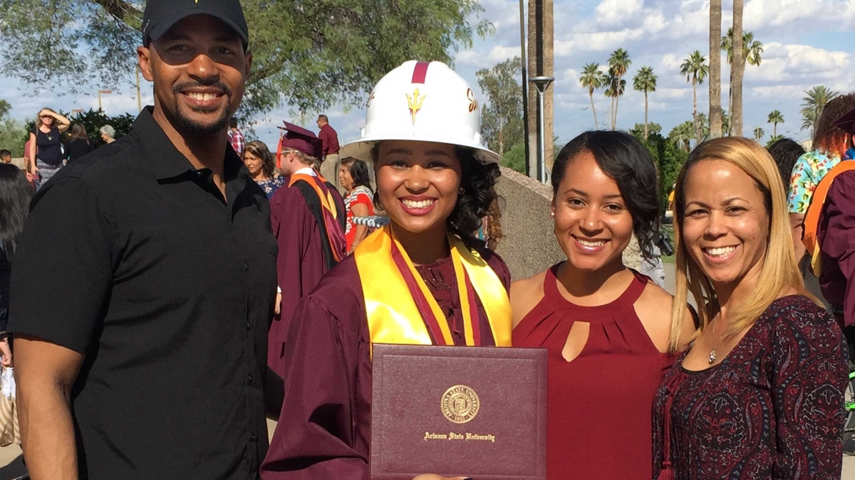 A woman in a graduation gown and construction hat stands with her family at a 2017 ASU graduation