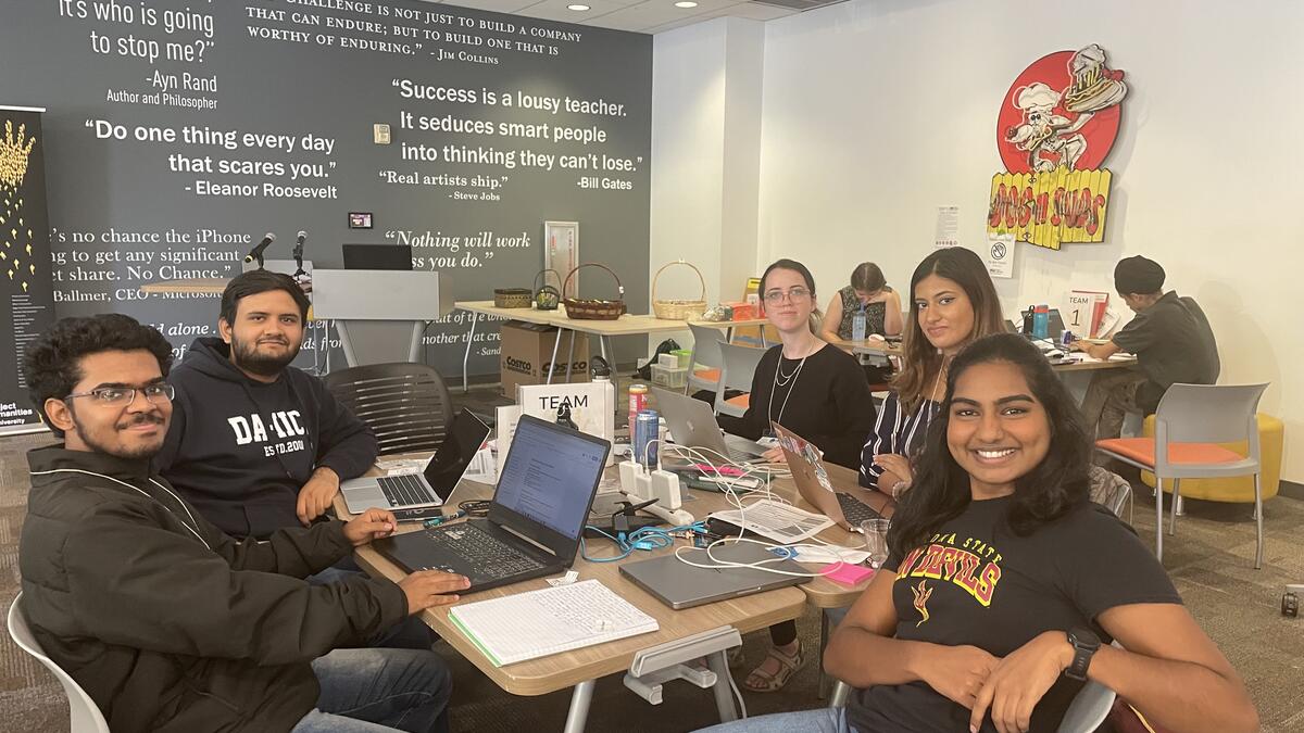 Smiling college students seated around a table with laptops and notebooks.