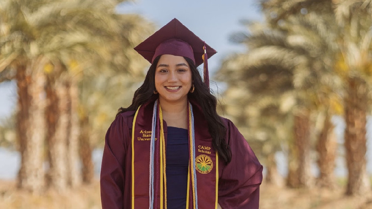 Vanessa Aguiar poses in an outdoor setting wearing her graduation gown, cap and stole.