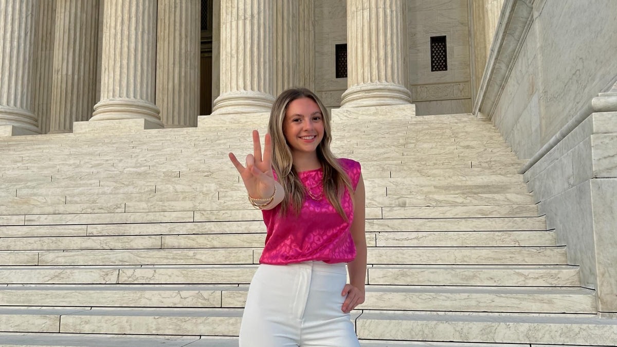 Logan Higgins on the steps of the Supreme Court doing the forks up hand gesture.