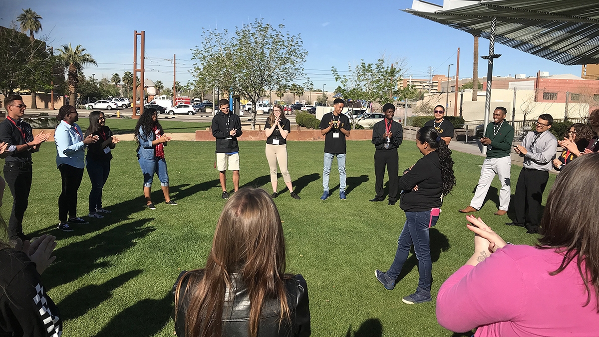 Parks and recreation professionals and students stand in a circle on the grass for an activity-based workshop