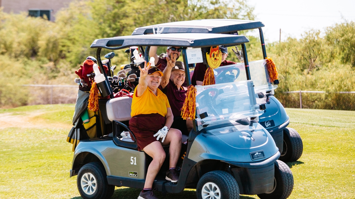 People dressed in marron and gold clothes sitting in a golf cart.