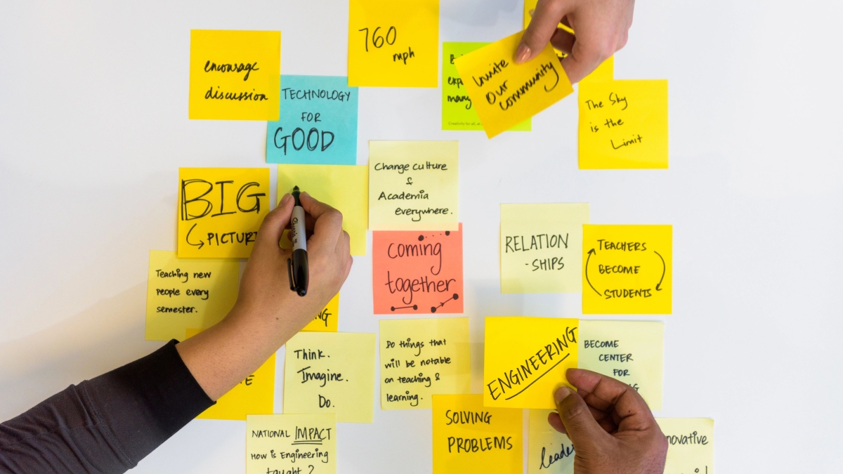 Three hands write ideas down and place sticky notes next to each other on a table 