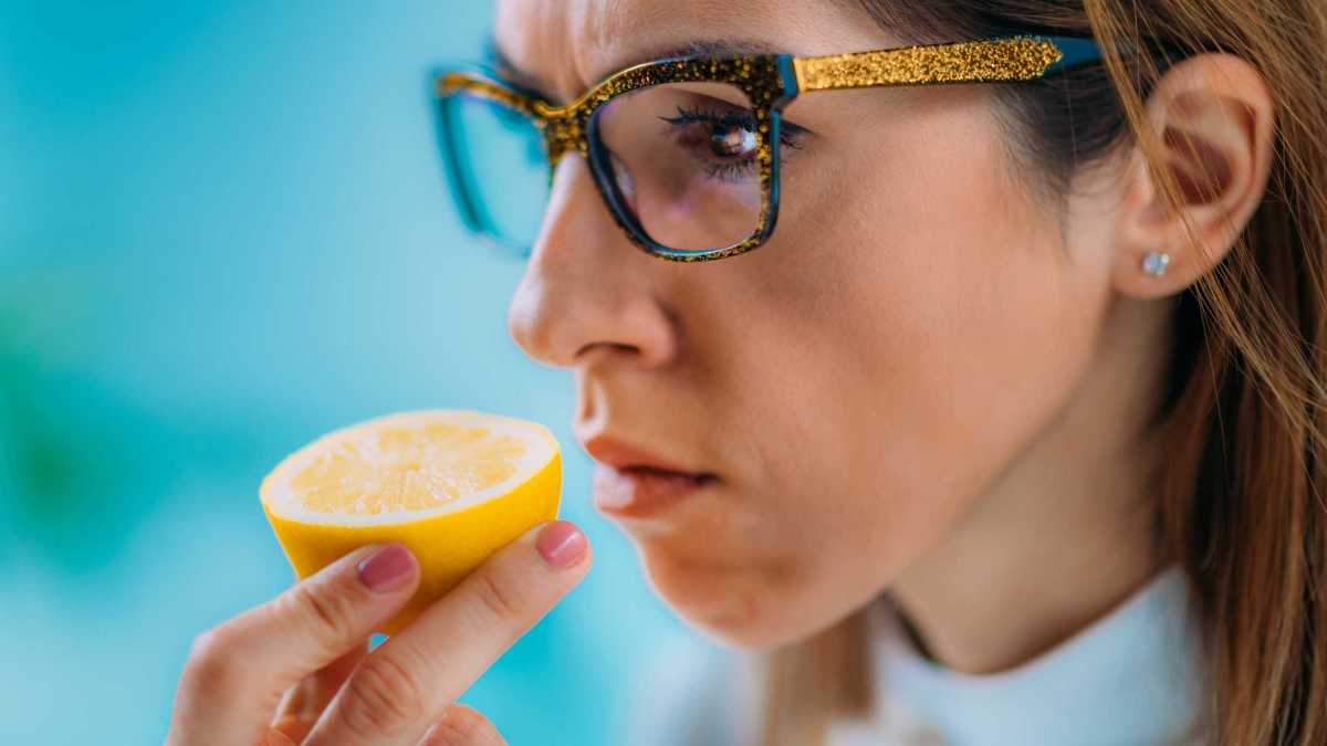 A woman looks serious or concerned as she smells a citrus fruit