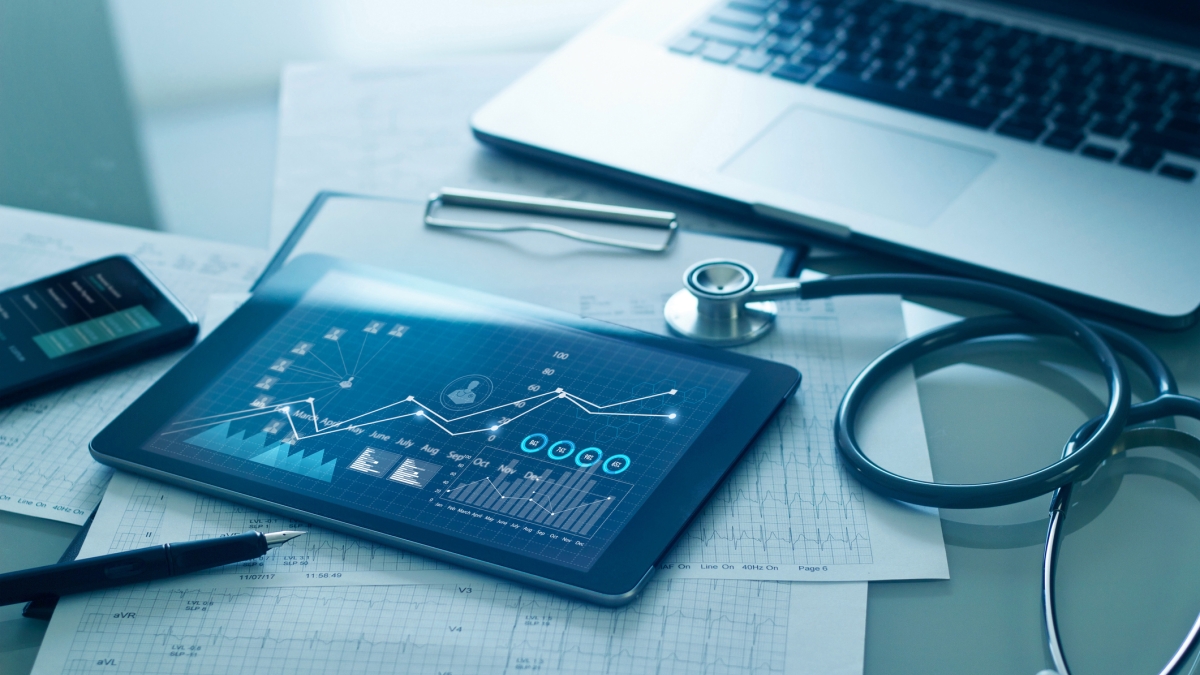 Stock photo showing medical charts, a stethoscope, a computer and a tablet with business charts