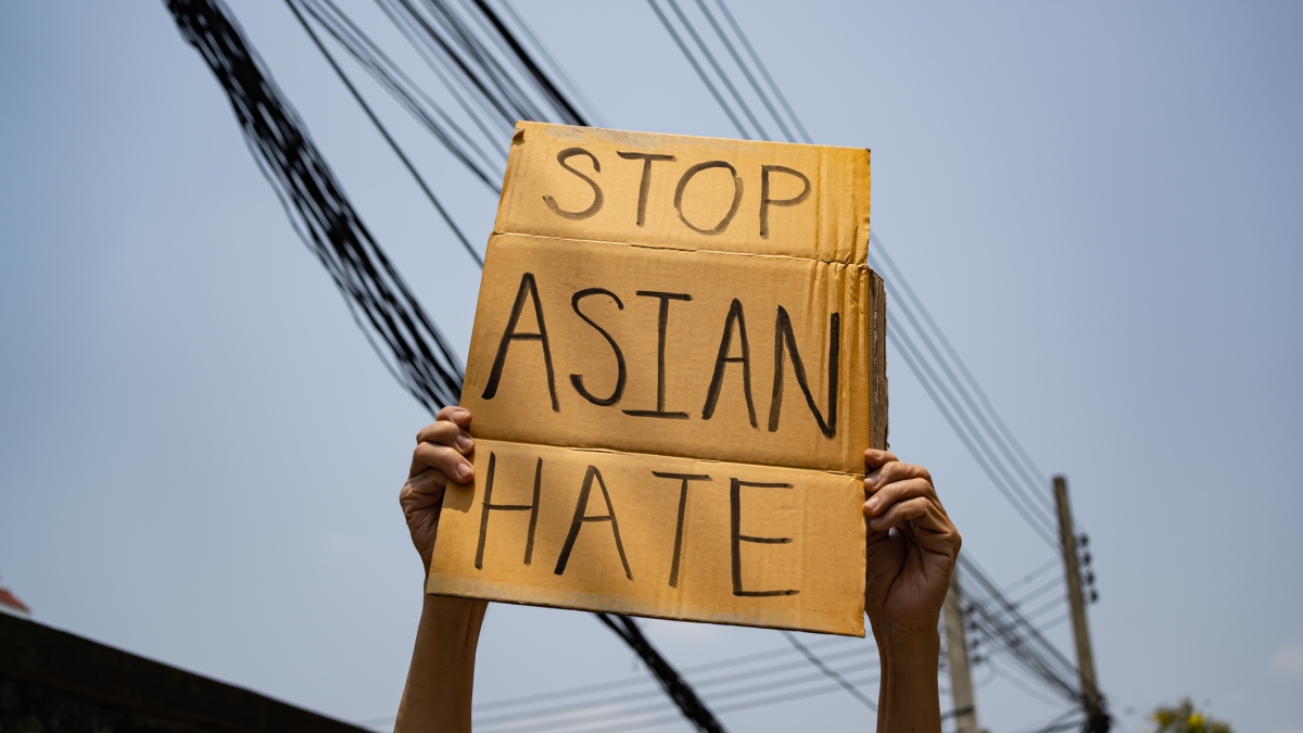 Hands hold up a cardboard sign that says Stop Asian Hate