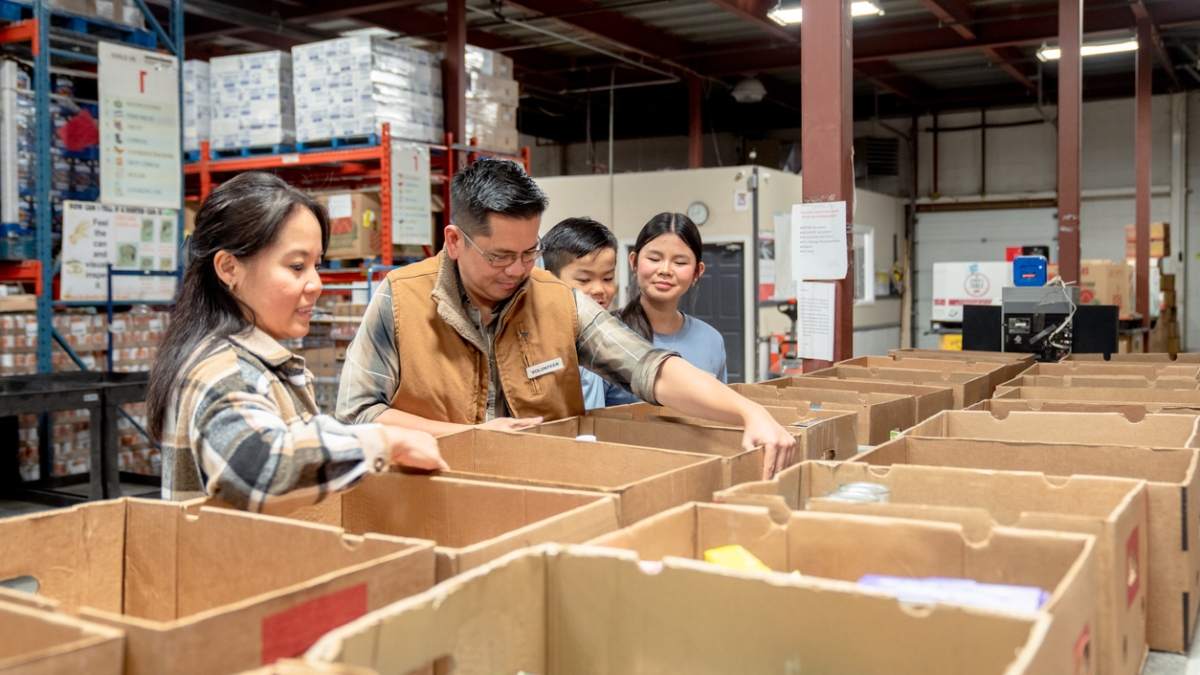People packing items into boxes for a food bank in a warehouse setting.