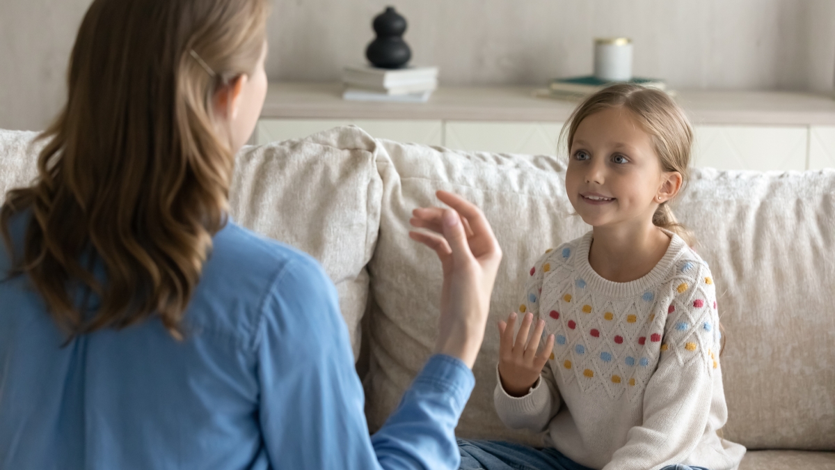 Woman gesturing with her hands during a speech therapy session with a child.