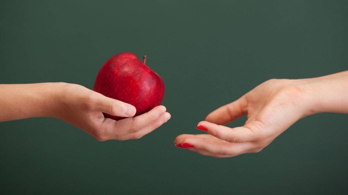 A child's hand gives an apple to an adult's hand