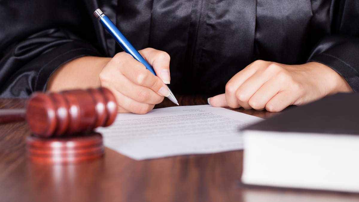 Hands of a female judge in a robe, writing on a piece of paper.