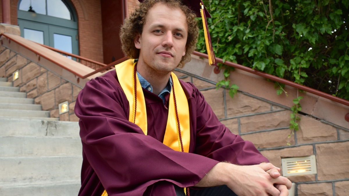 Jimmy Arwood sits on the steps of Old Main in his grad cap and gown
