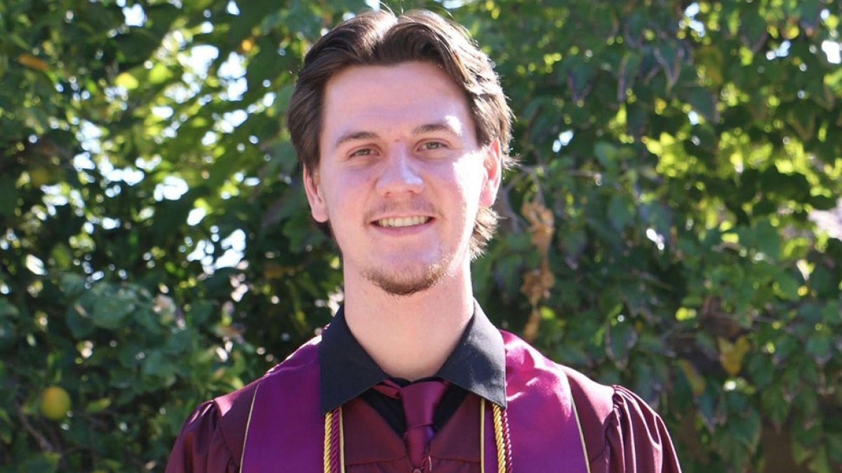 College of Health Solutions graduate Jacob Patterson wearing his graduation gown and stole and smiling at the camera in an outdoor setting.