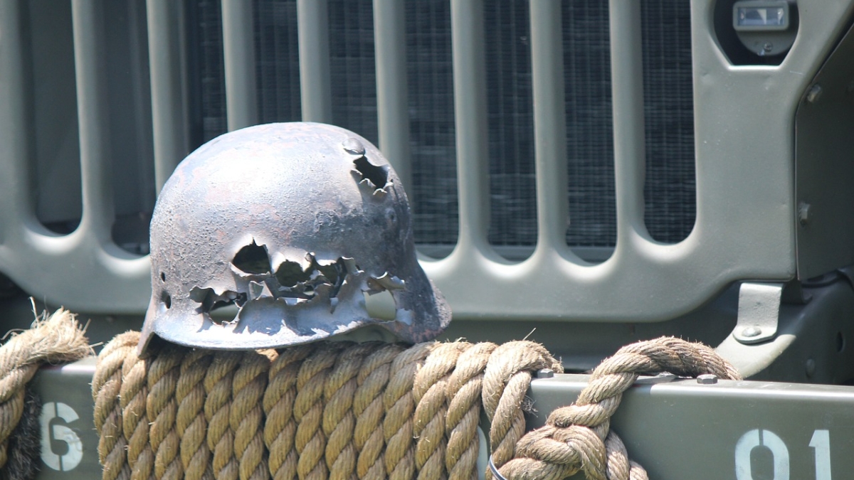 Close-up image of the front of a battered helmet resting on the front bumper of a Jeep.